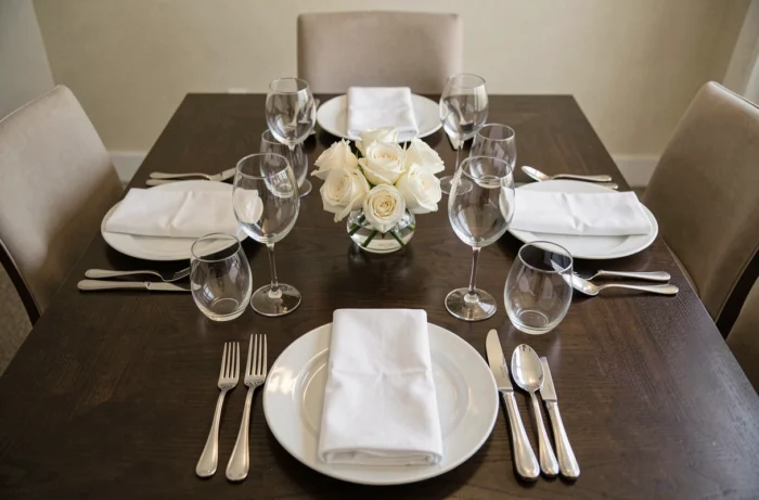 Table de dîner élégamment dressée vue de dessus avec verres en cristal, assiettes en porcelaine et couverts en argent sur nappe blanche